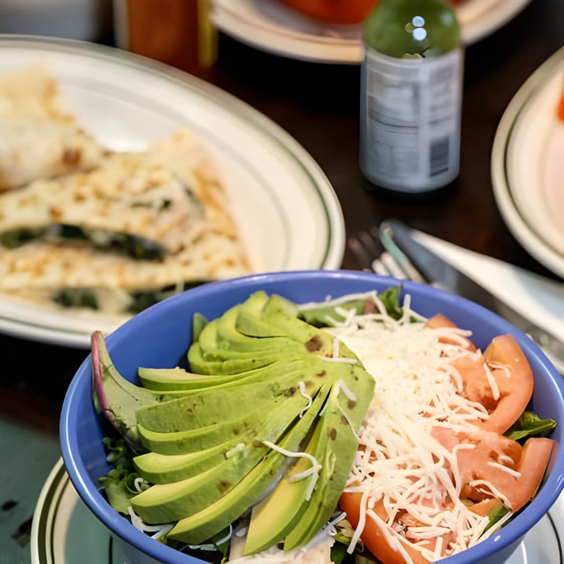A blue bowl of Tinga Fresh Mexican salad with avocado, tomatoes, and shredded cheese.