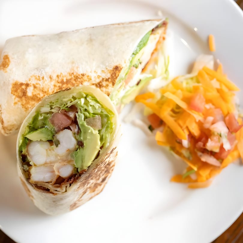 Two Tinga Fresh Mexican shrimp burritos, one cut open to show shrimp, avocado, and lettuce, with a side salad.