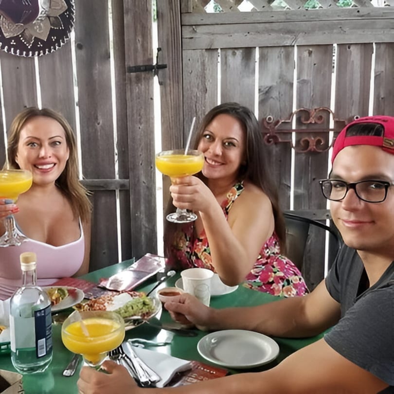 Three happy diners at Tinga Fresh Mexican, two women toasting with margaritas, and a man smiling.