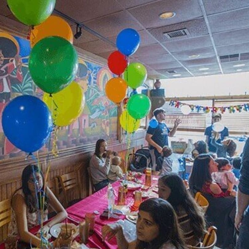 A lively birthday party at Tinga Fresh Mexican, with colorful balloons and guests celebrating.