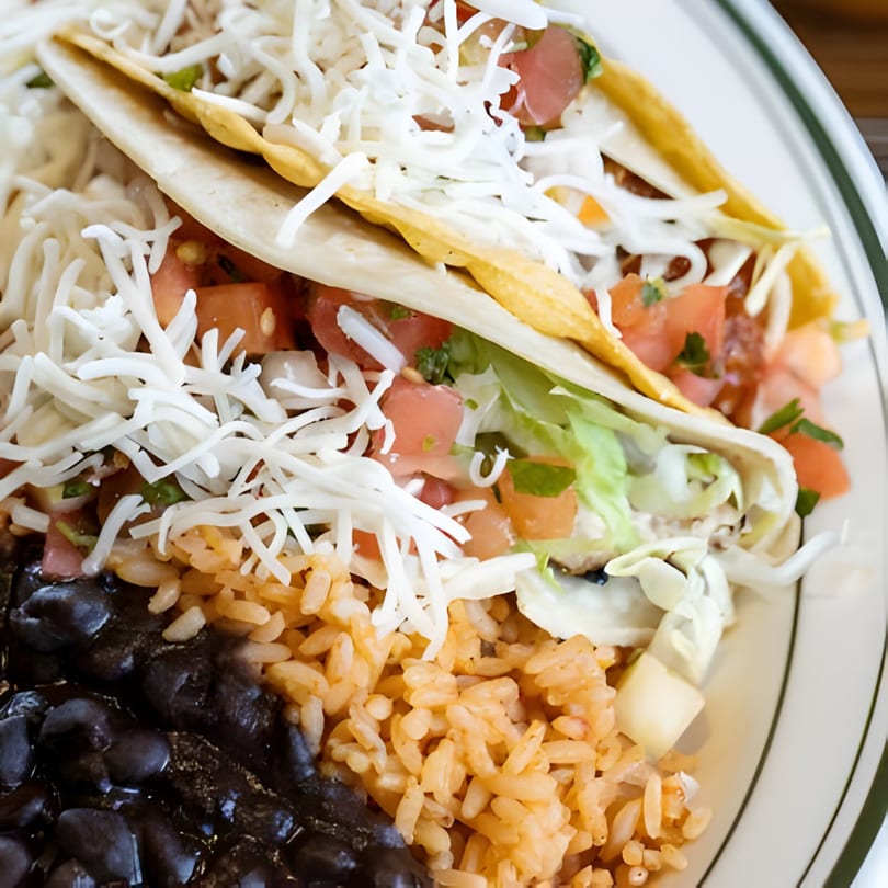 Two Tinga Fresh Mexican tacos with shredded cheese, lettuce, and tomatoes, served with rice and black beans.